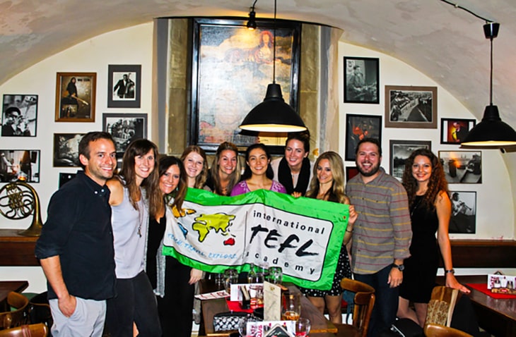 Graduates from the International TEFL Academy holding a TEFL banner, celebrating online certification success for teaching English abroad.